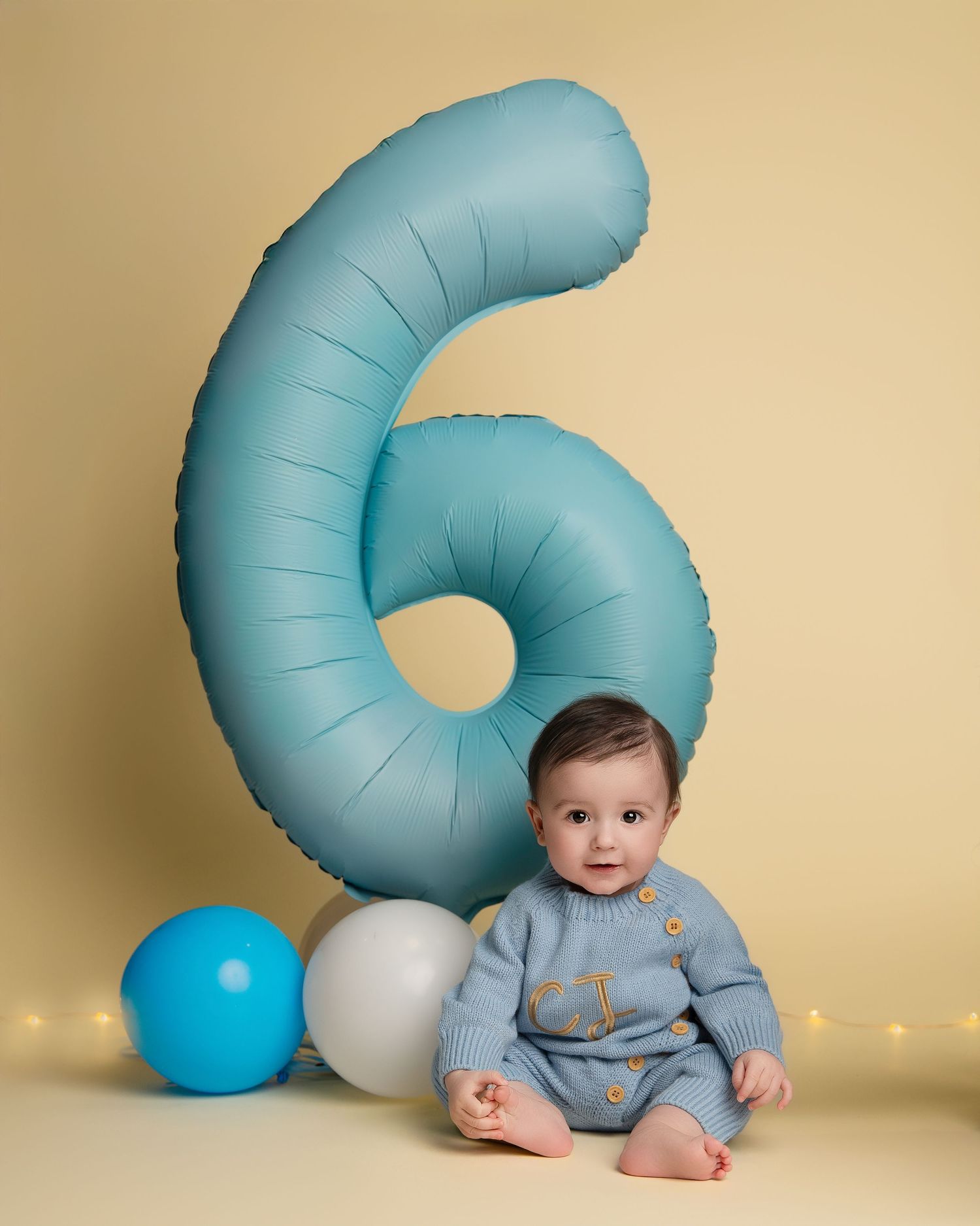 Baby in blue romper with large number 6 balloon for six month milestone photo.