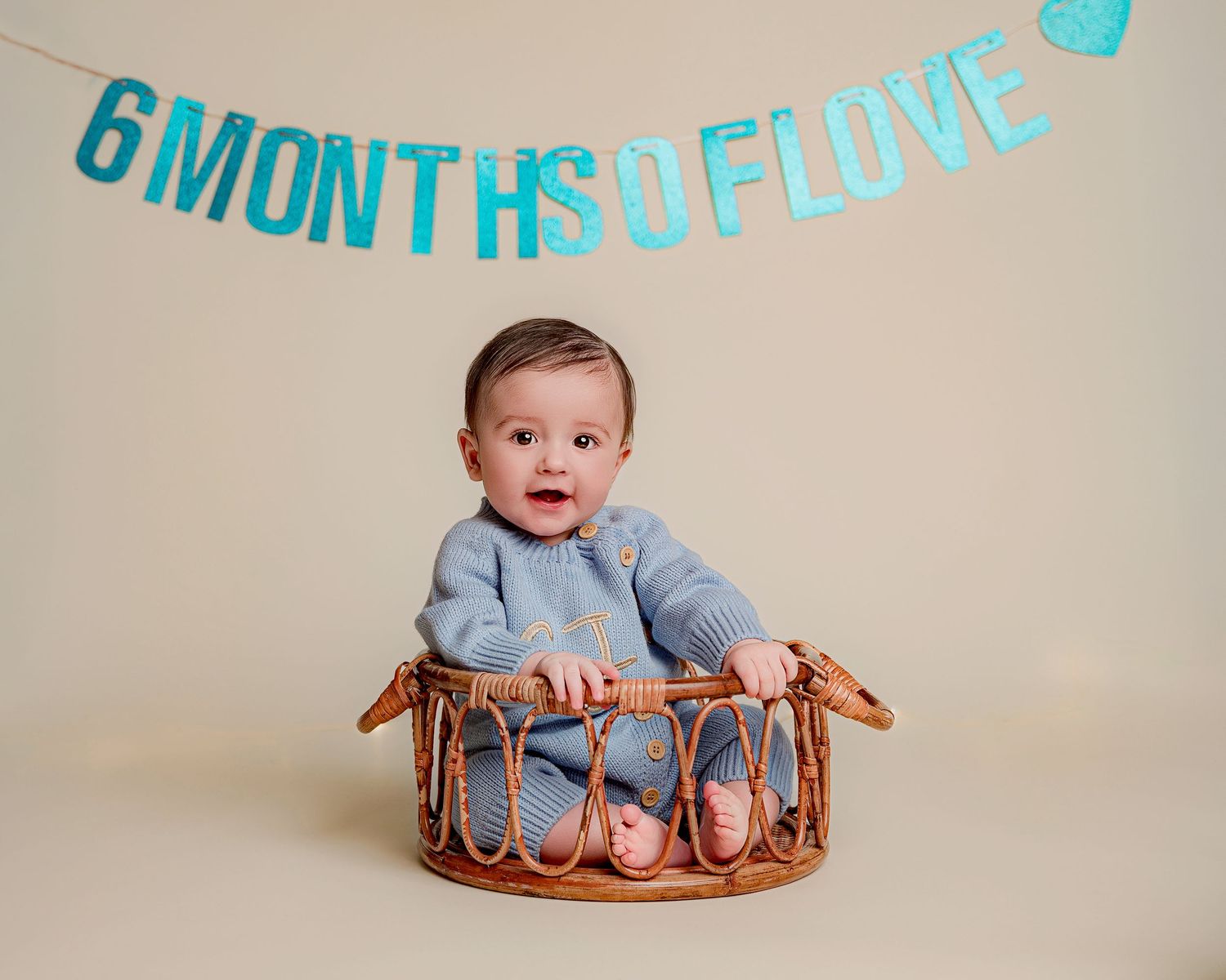 Baby in blue outfit sitting in basket with turquoise '6 months of love' banner.