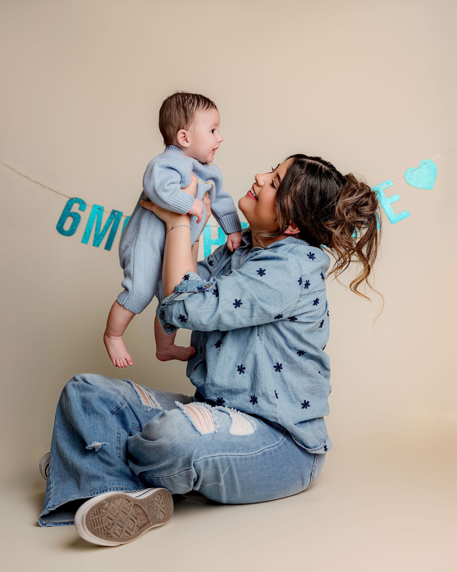 Mother and baby in matching blue outfits posing with milestone banner.