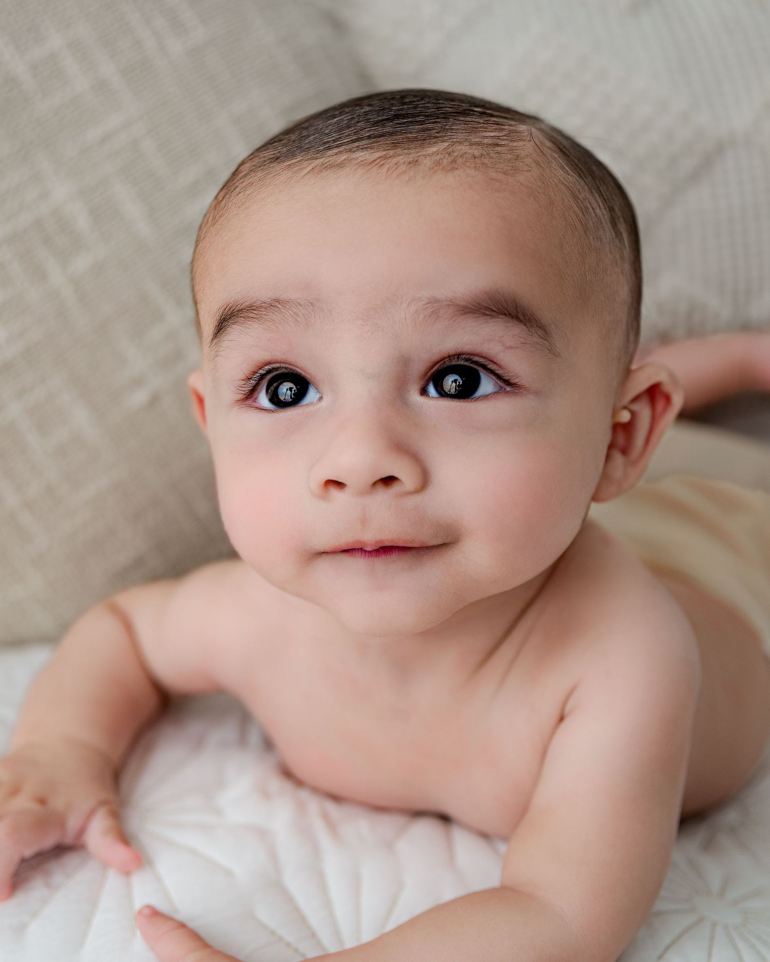 Infant rests on white linens with bright eyes and sweet expression.