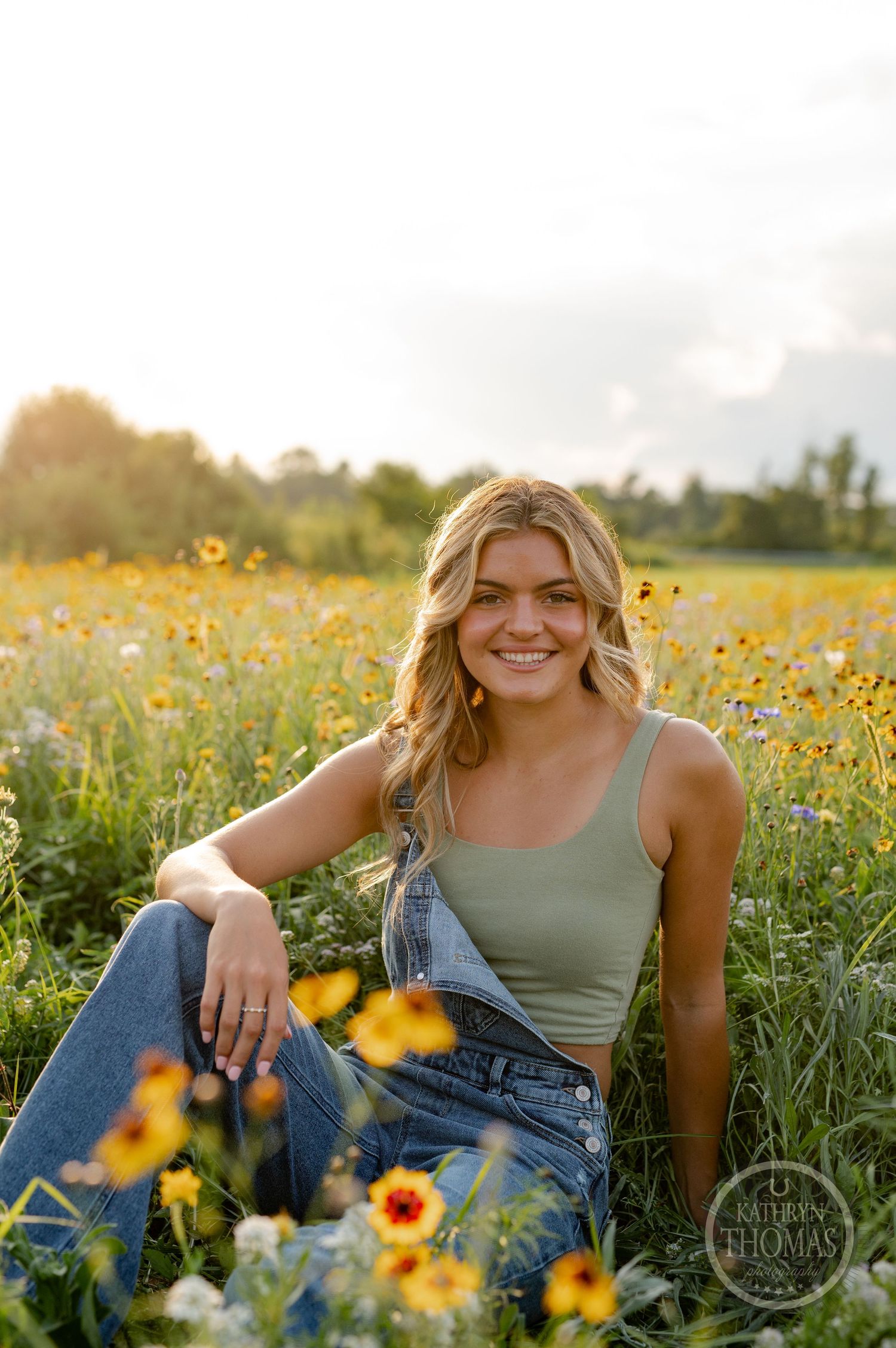 A casual summer portrait among yellow wildflowers with someone wearing overalls and a green tank top.