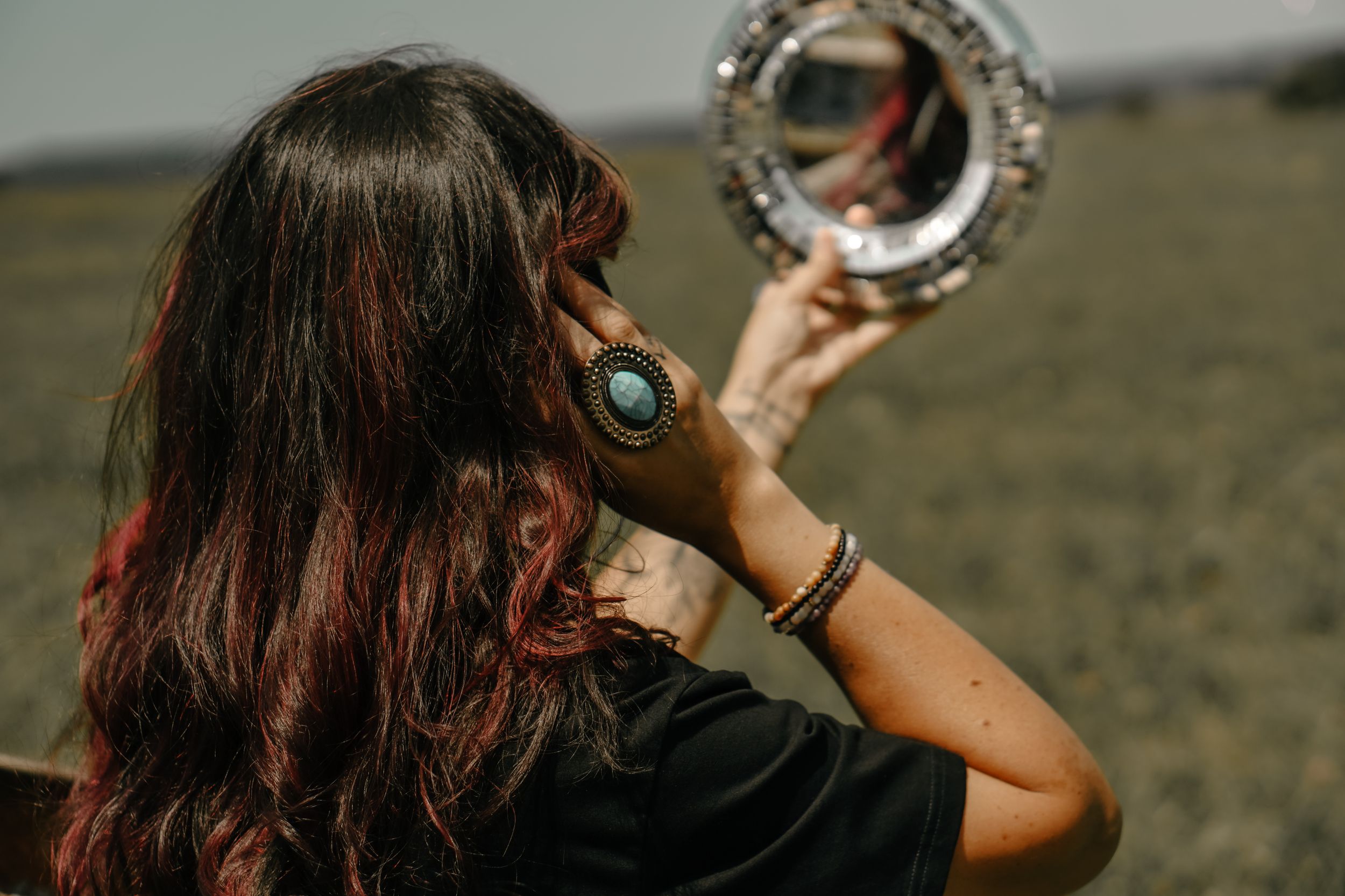 Person with long dark hair holds up a reflective silver disc in an outdoor setting.