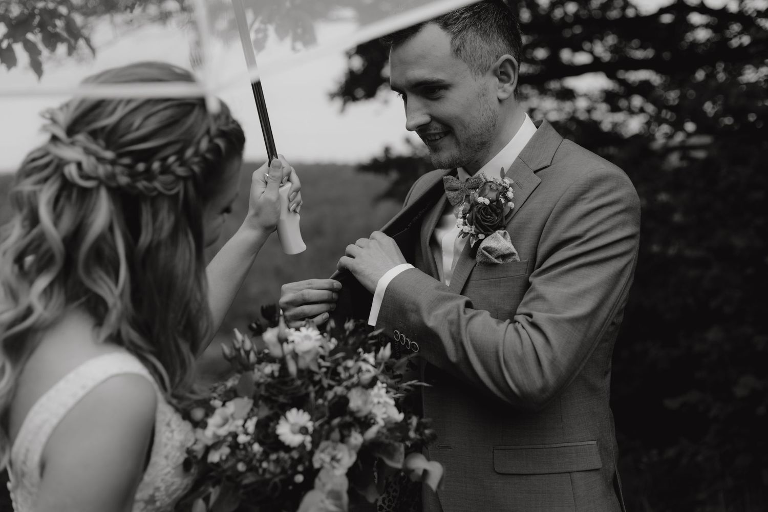Black and white photo of couple exchanging rings during outdoor ceremony.