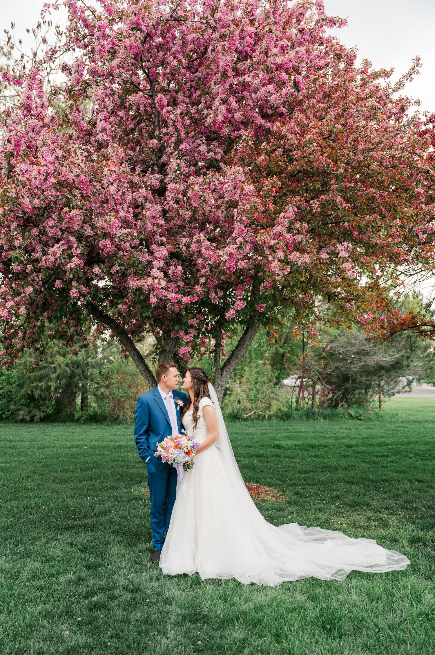 Wedding couple poses under a pink flowering tree during spring photo session.