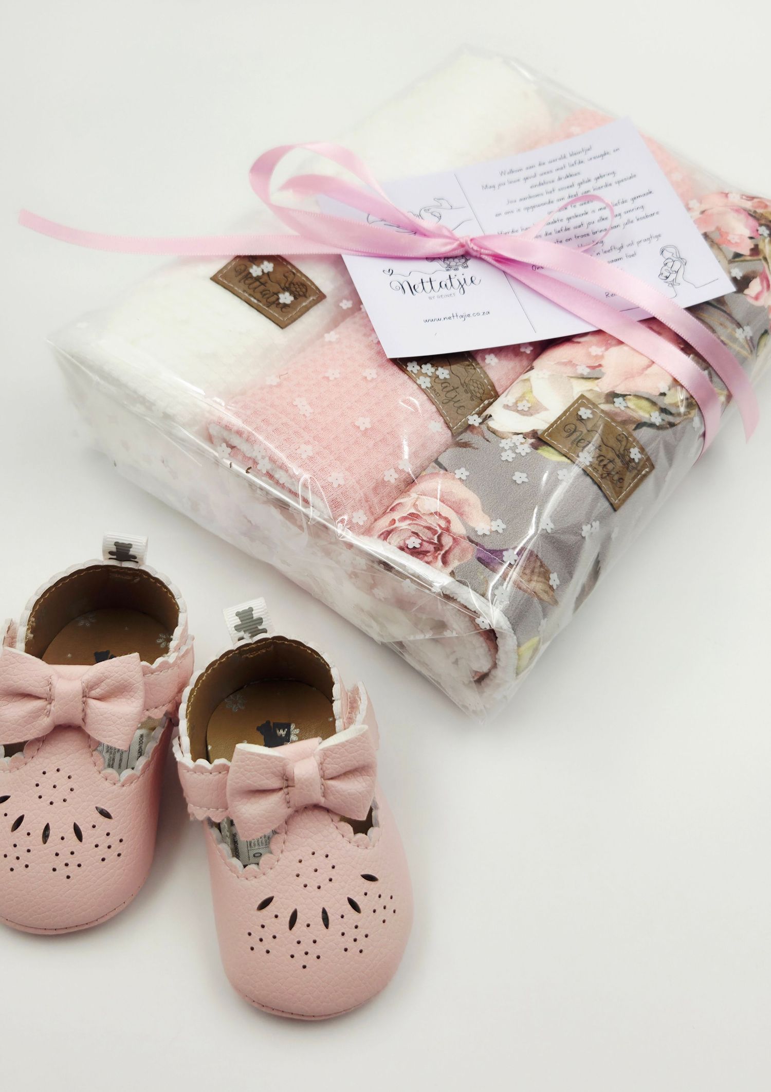 Pink leather baby shoes displayed with matching floral blankets tied with pink ribbons.