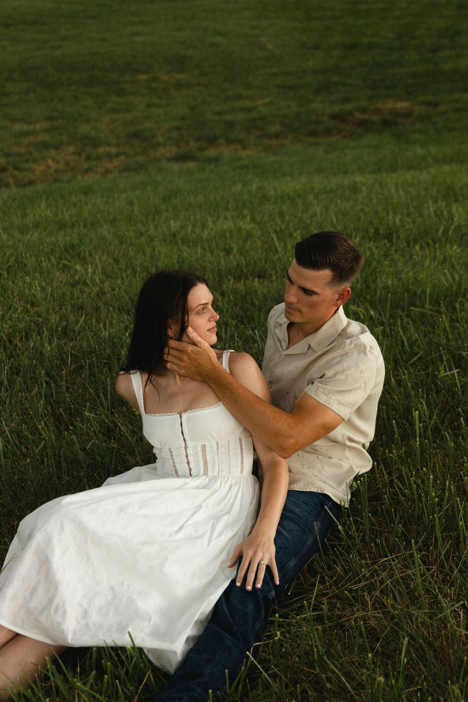 A romantic couple lounging in a grassy field at golden hour.