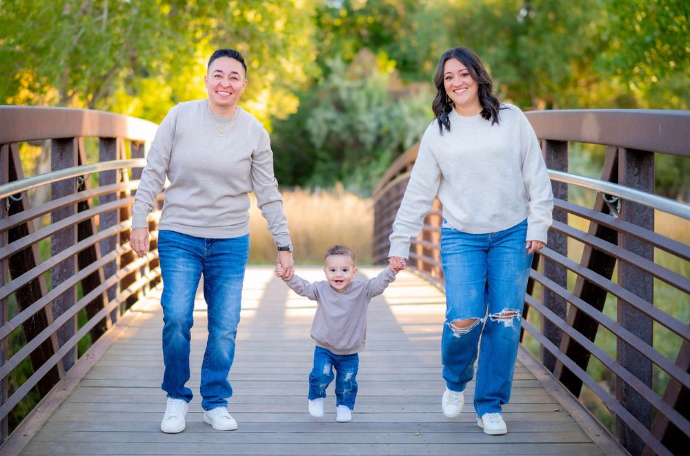 Family walking together on wooden bridge pathway surrounded by autumn trees.