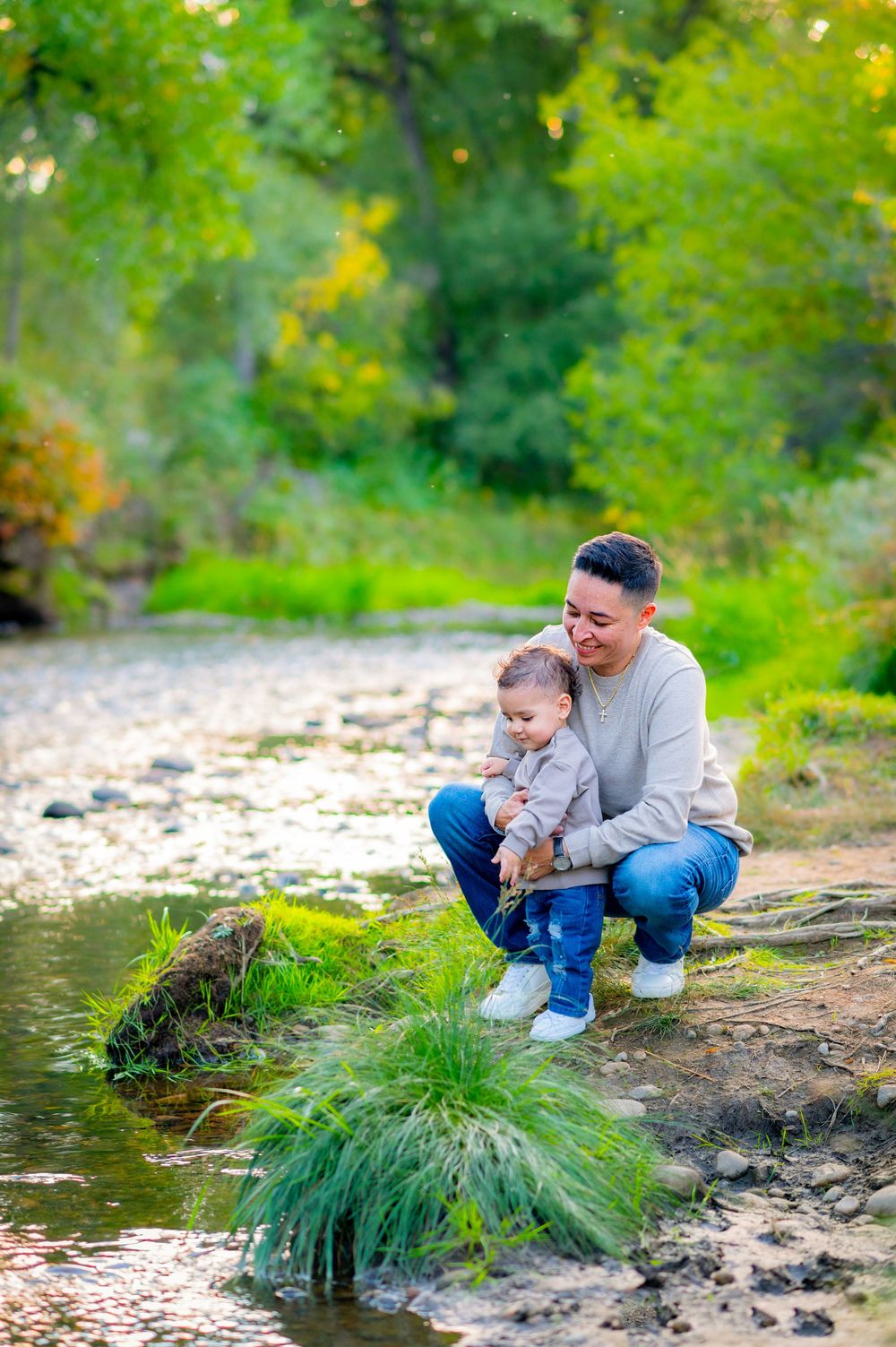 Parent and child exploring creek bank together on sunny autumn day.
