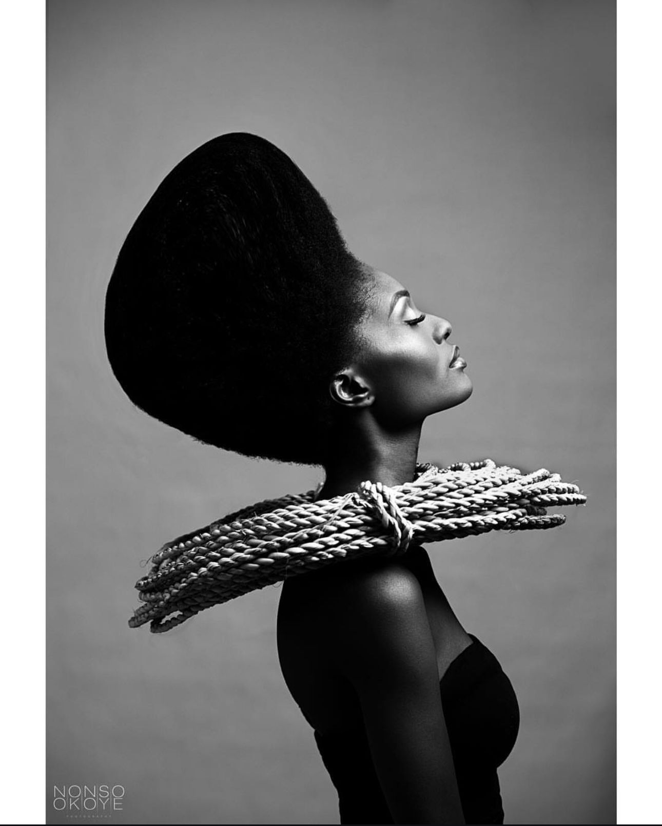 Striking black and white portrait featuring sculptural hairstyle and ornate neckpiece.