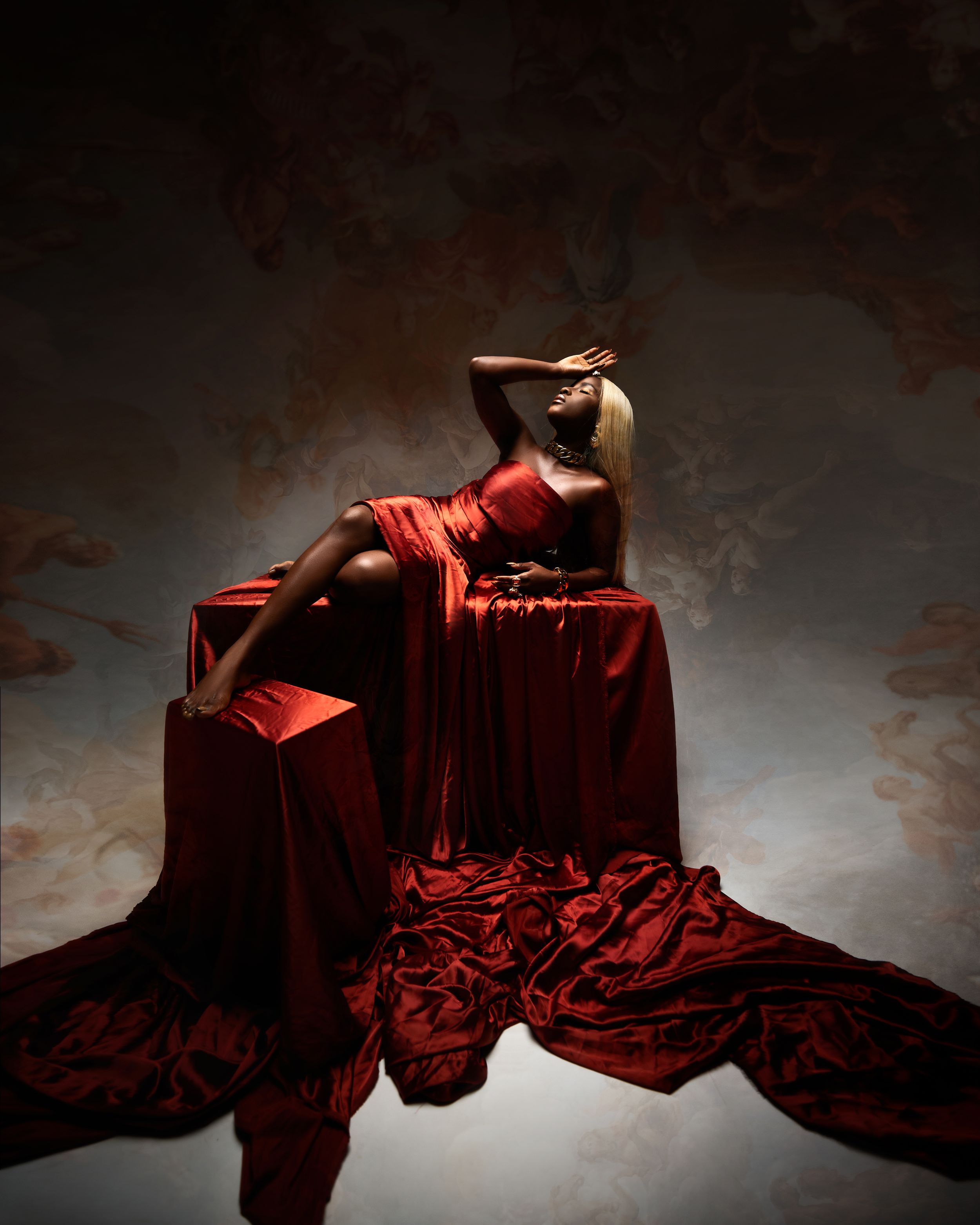 Dramatic portrait with flowing red fabric against dark background.