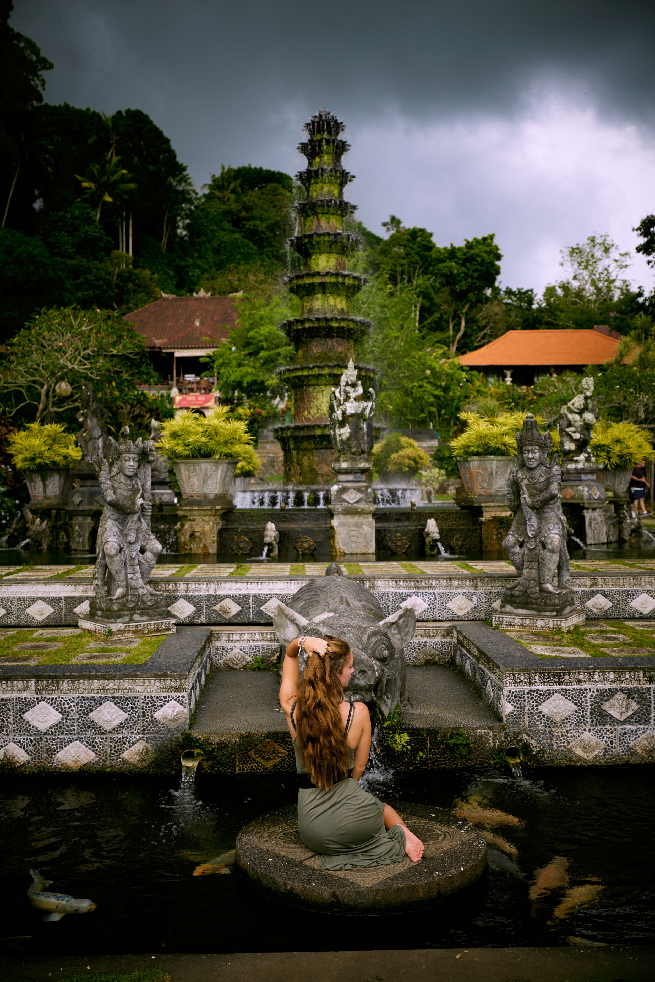 Ancient temple complex with ornate pagoda and stone statues under stormy sky.