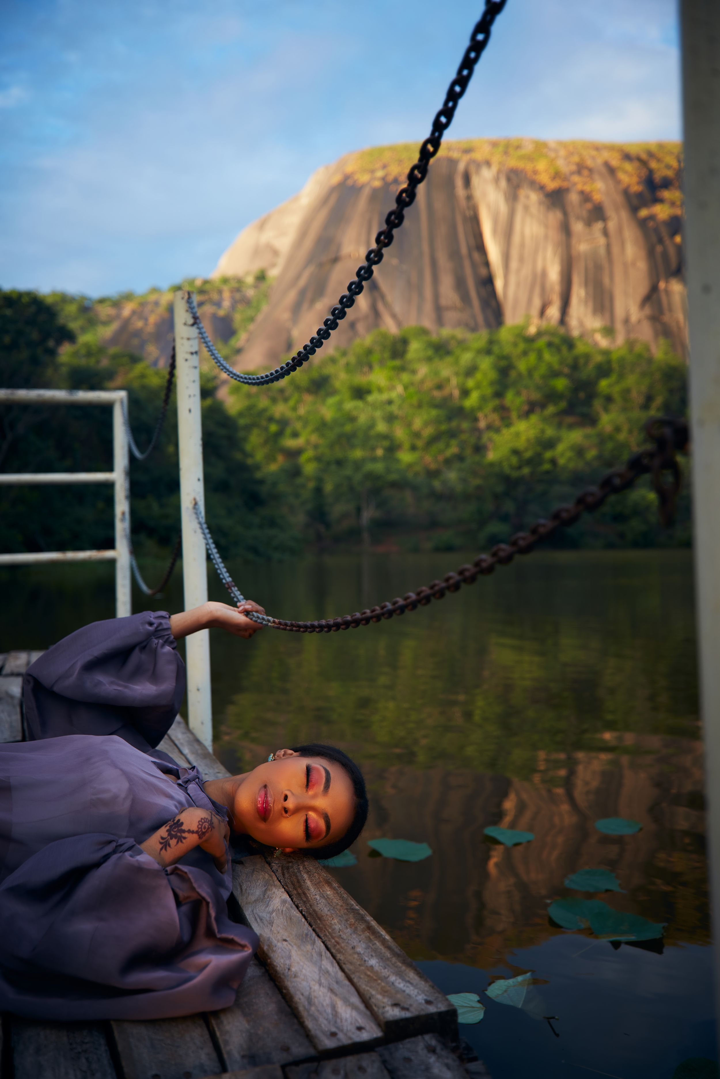 Person resting on bench near large rock formation and lake.