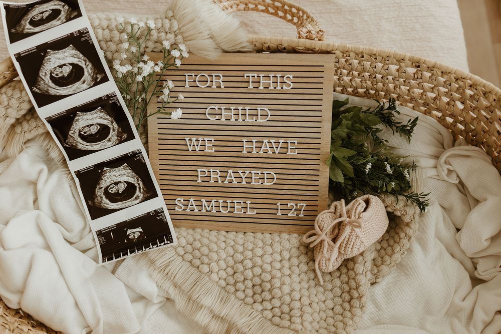 Pregnancy ultrasound photos arranged with letter board signs and floral decorations in a sepia-toned collage.