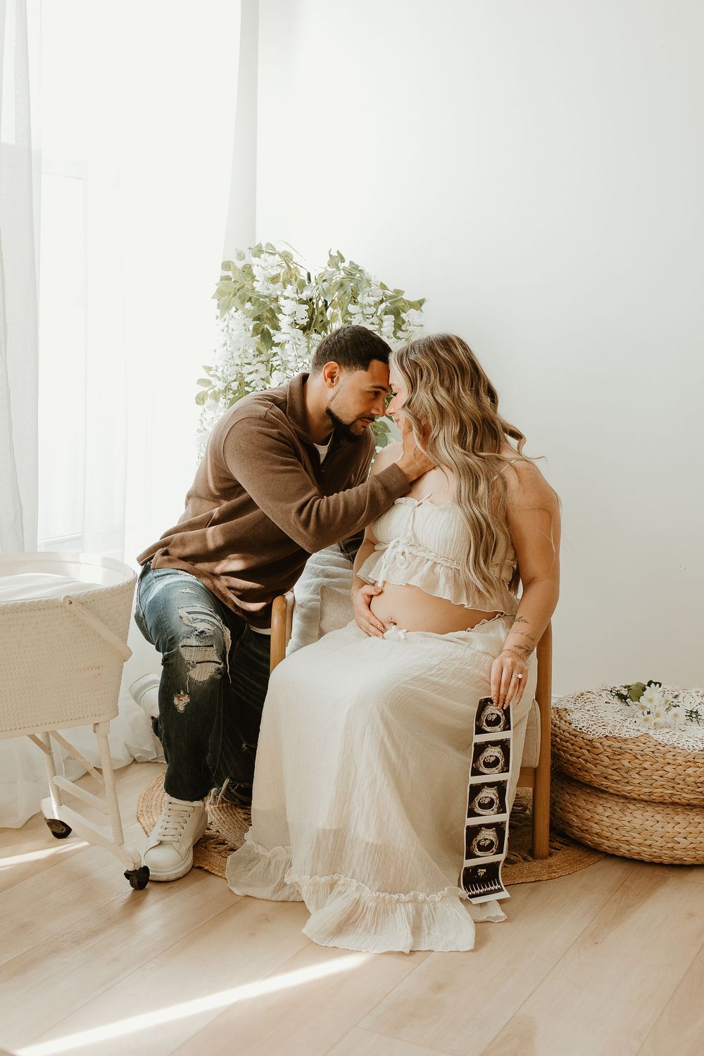Minimalist maternity session showing couple sitting together in sunlit white room.