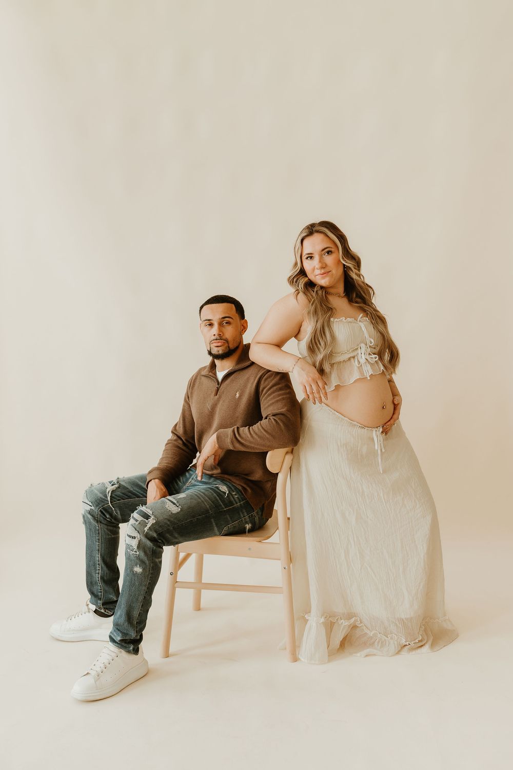 Natural light maternity portraits against neutral backdrop with wooden chair.