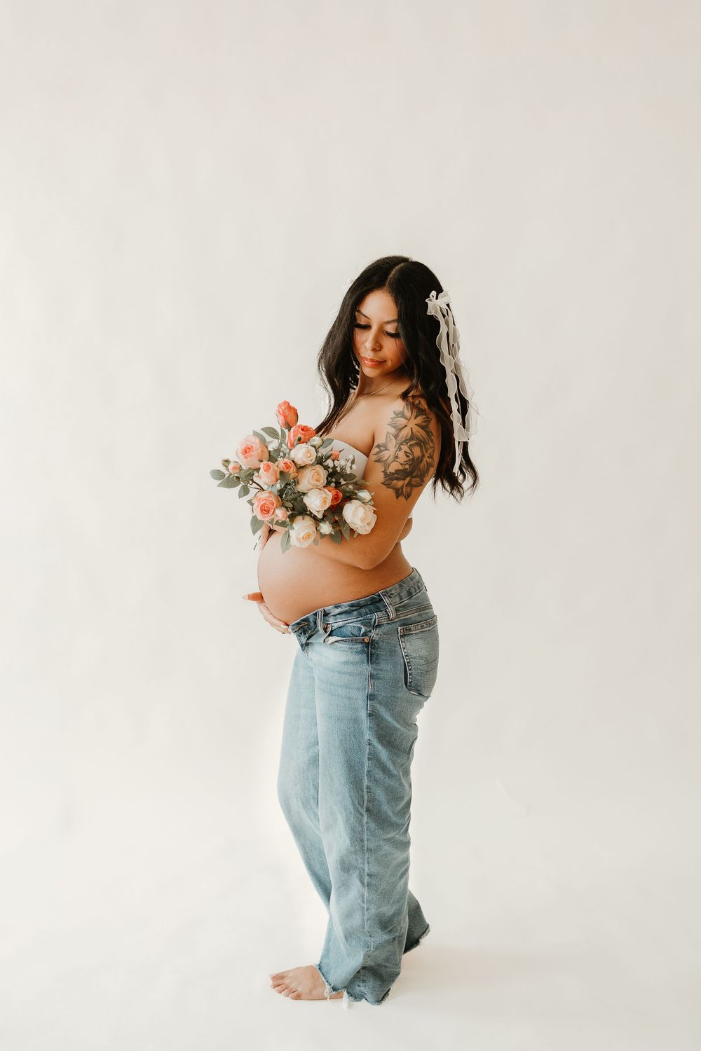 A series of maternity photos showing someone in overalls holding pink flowers against a white studio backdrop.