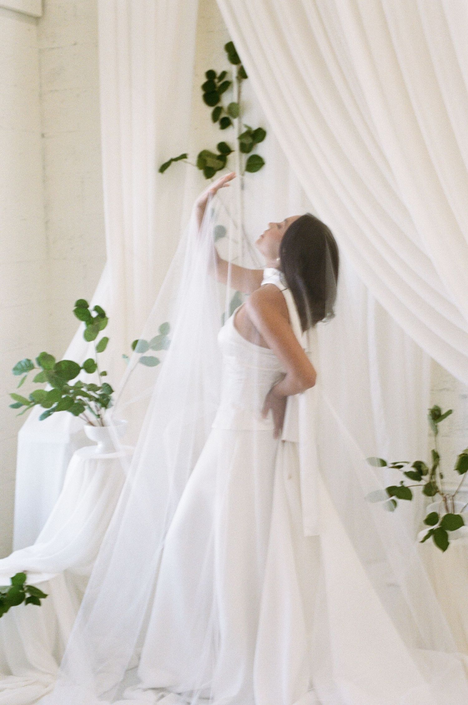 A classic, candid, film bride in Jupiter, South Florida, wearing a vintage, handmade dress pose under the vail surrounded by natural plants.