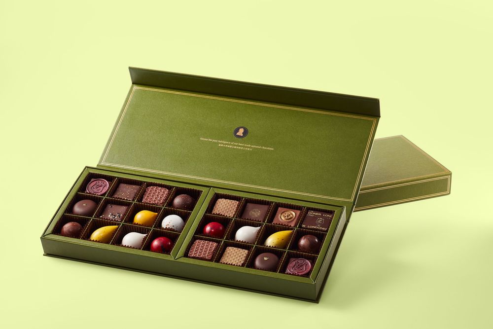 Elegant green gift box filled with assorted luxury chocolates, including pralines and truffles, on a light green background.