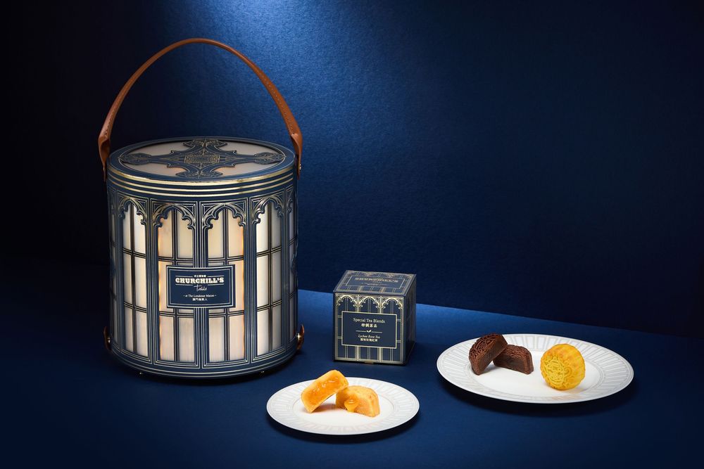 Elegant navy blue tin canister with leather handle beside small boxes of gourmet chocolates and candied fruits on white plates.