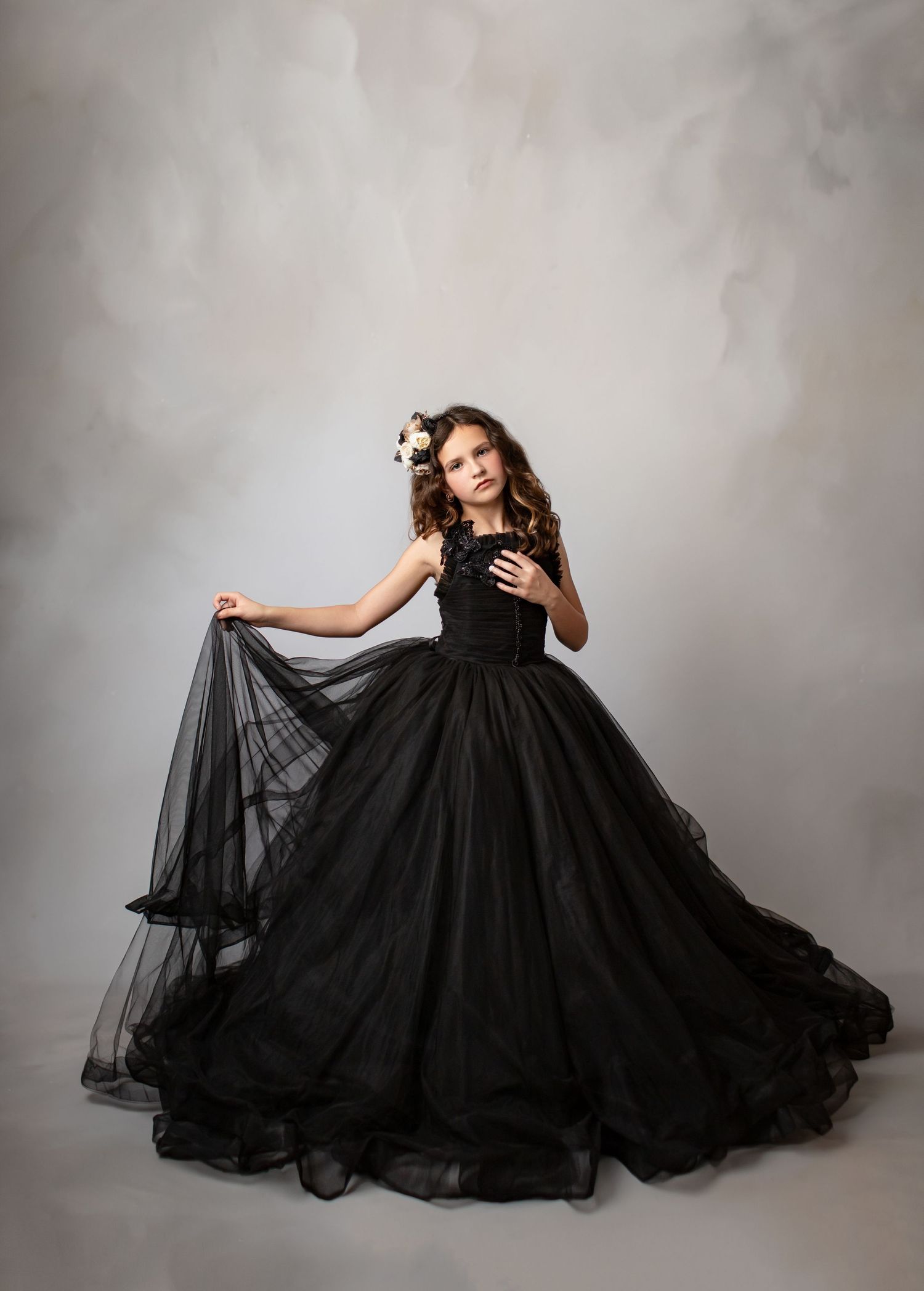 Dramatic portrait featuring flowing black tulle gown with full skirt against light studio backdrop.