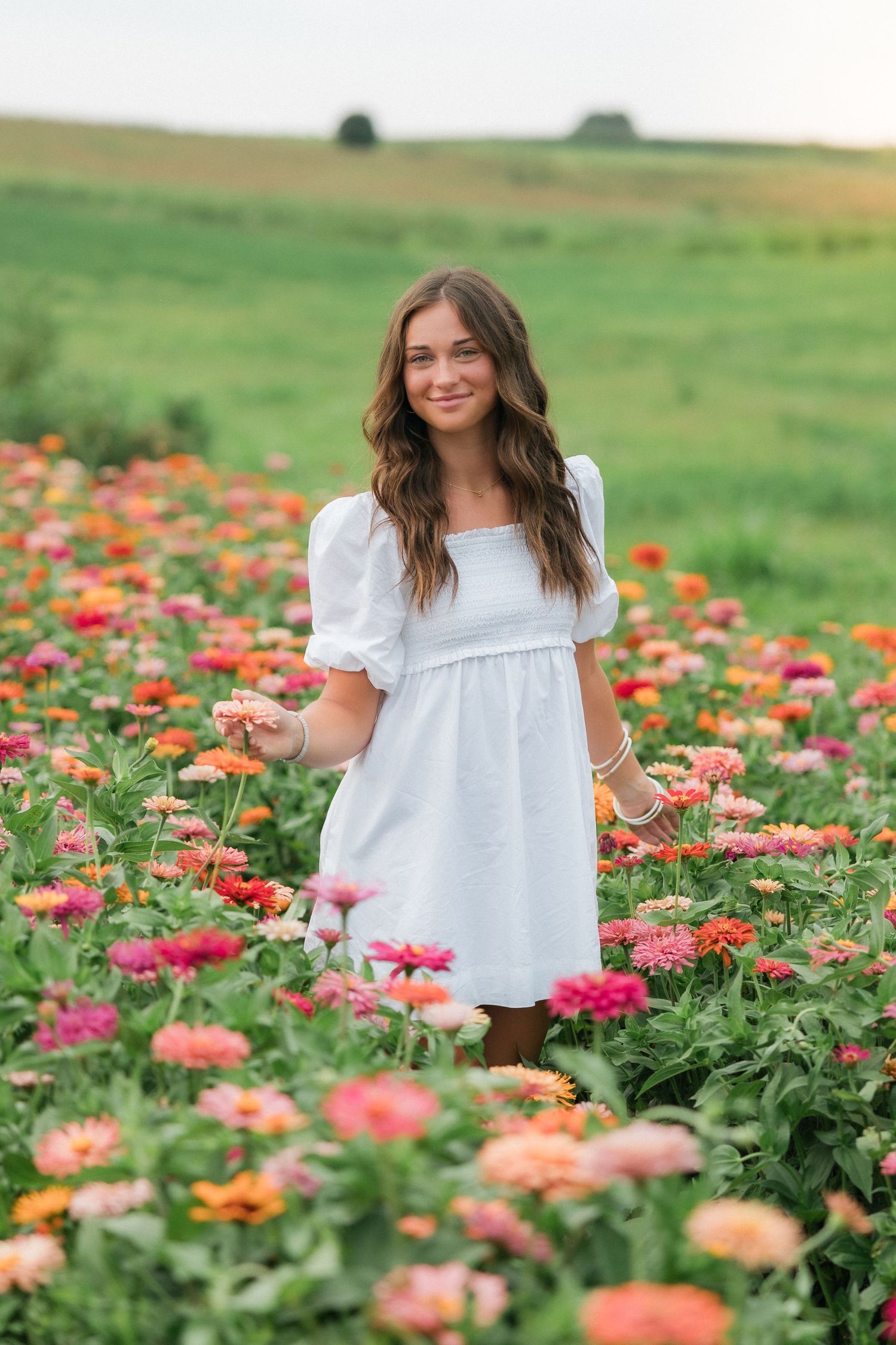 A person in a white dress stands in a field of colorful zinnia flowers.