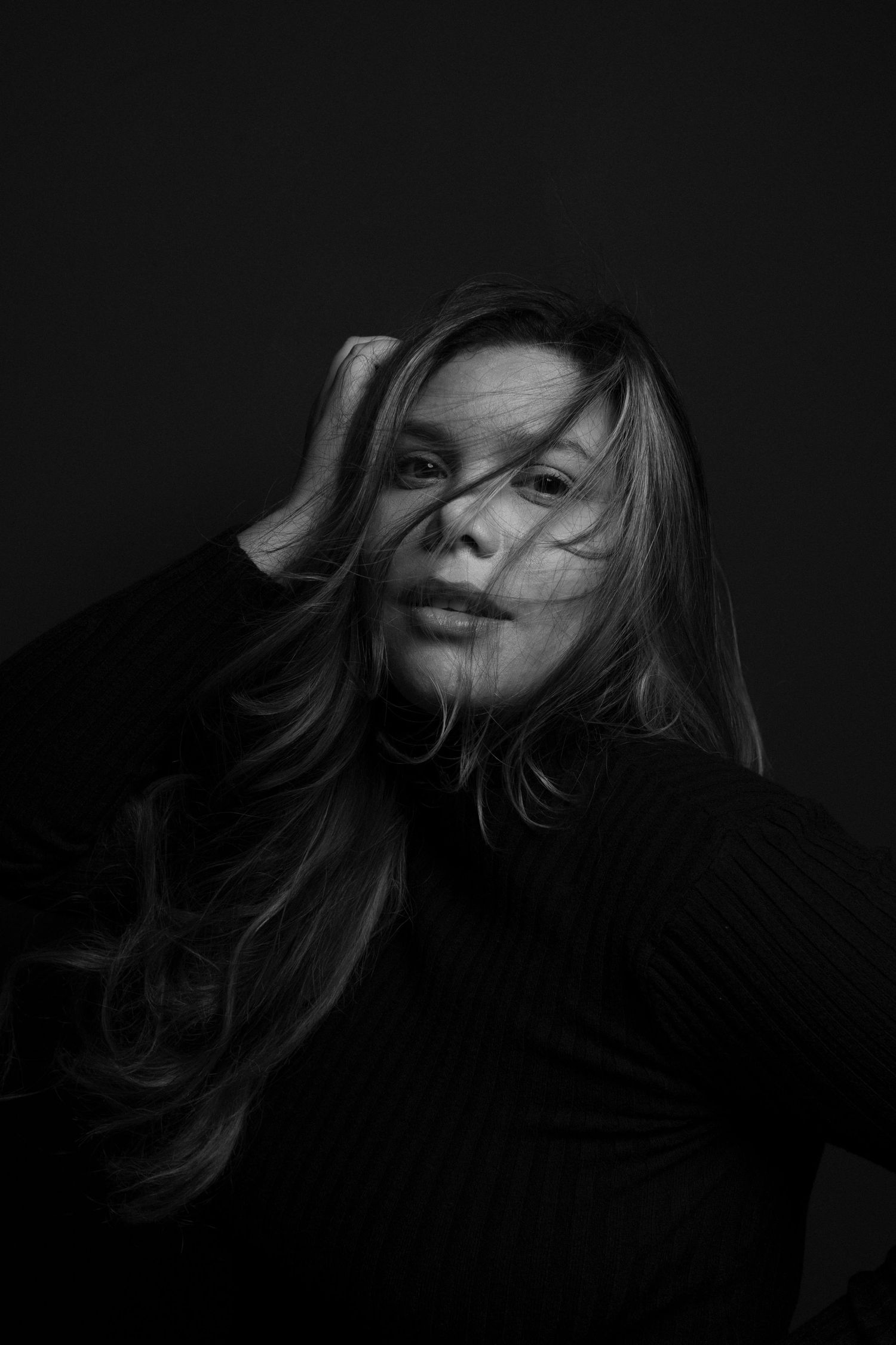 Photographer holds camera while posing under modern lighting fixture.