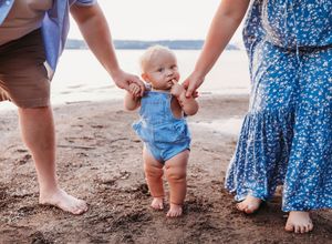 Closeup of bare feet walking on sandy beach in summer, showing multiple pairs of feet in casual attire.