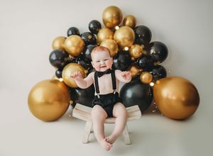 Milestone photo series showing baby's growth with black and gold balloon decorations against white background.