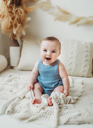 Baby in blue romper lies on cream lace blanket showing different expressions of joy and contentment.