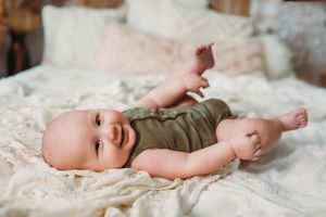 A series of connected photos showing a baby lying on soft white bedding wearing an olive green outfit.