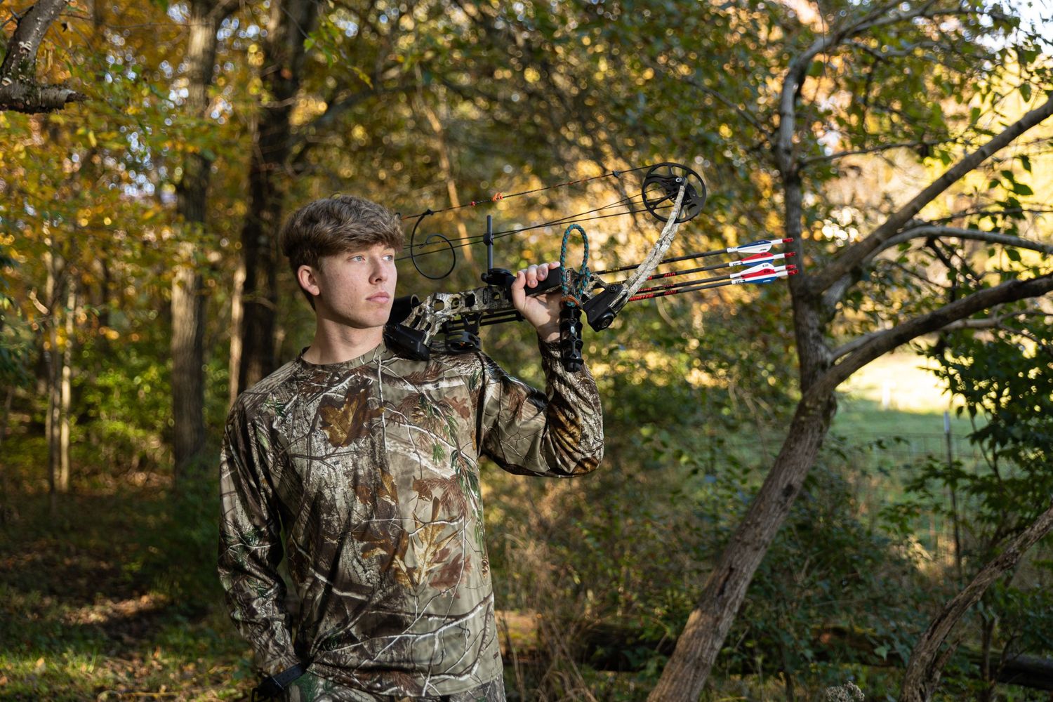 Camo wearing high school senior poses with his hunting bow while looking off into the distance.