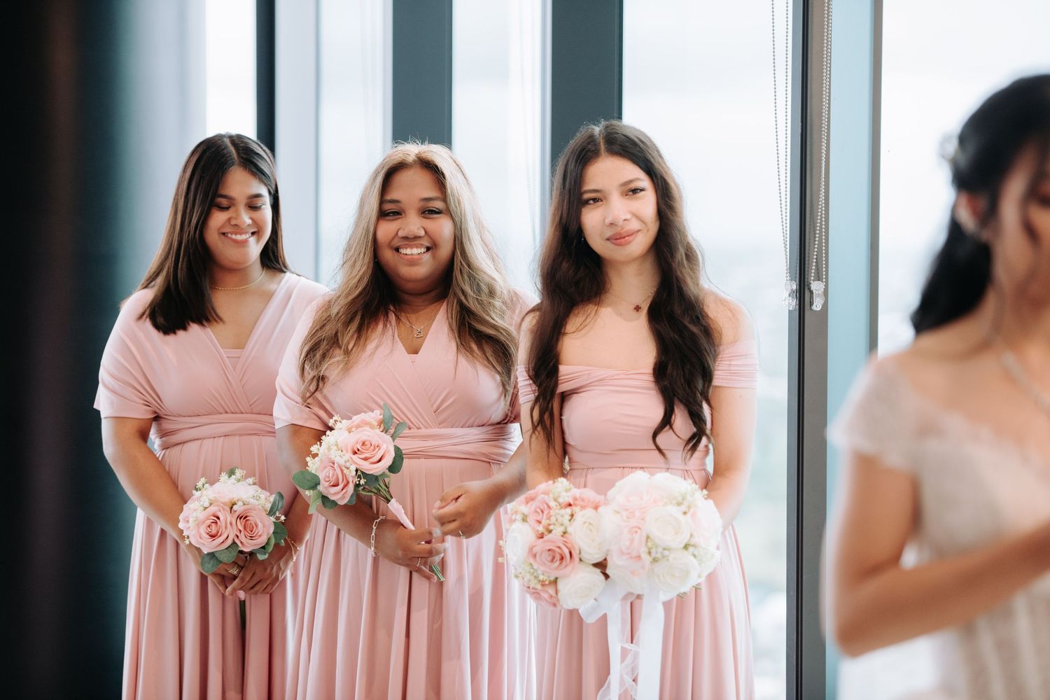 Bridesmaids in blush pink dresses holding bouquets during wedding ceremony.