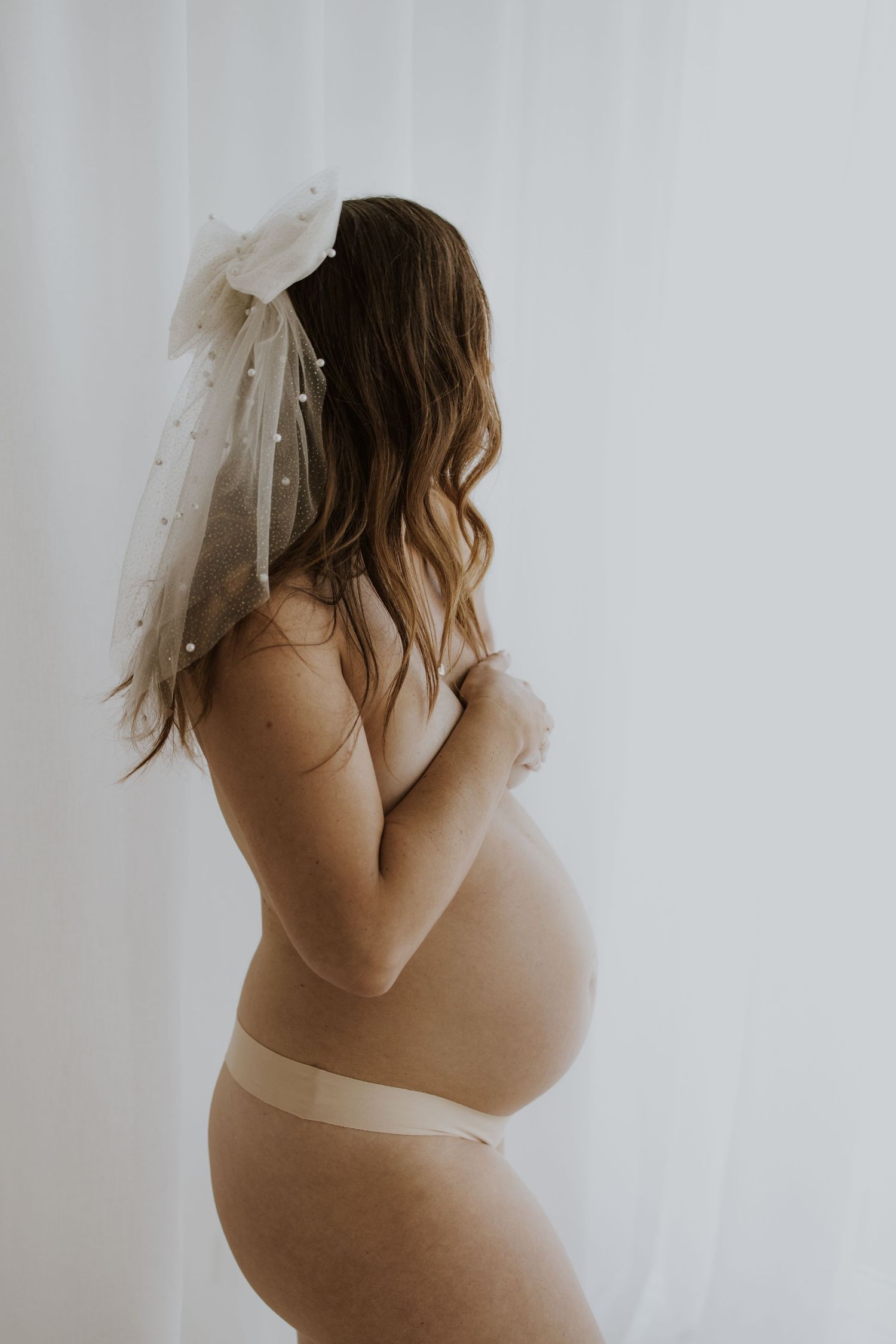 A side profile of an expectant mother wearing a bridal veil in a minimalist maternity photo.