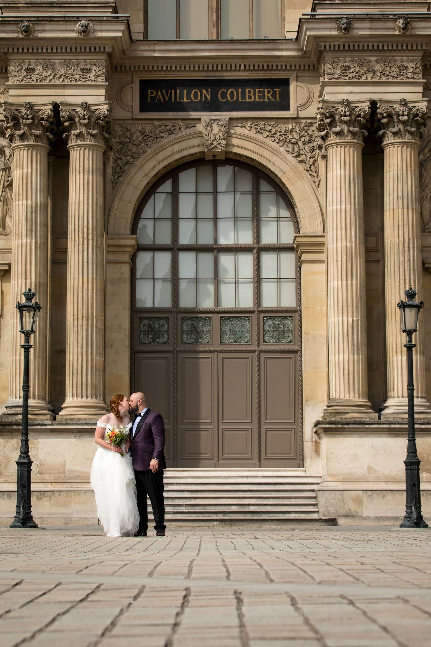 Laughter fills the air as a newly married couple shares a kiss in front of the Louvre. Photo by Julien LB Photogra
