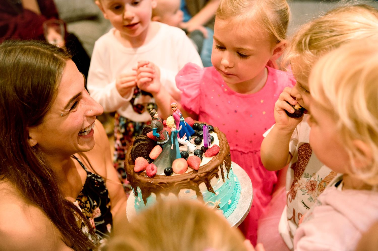 A small group gathers around a birthday cake with lit candles as they prepare to celebrate at a party.