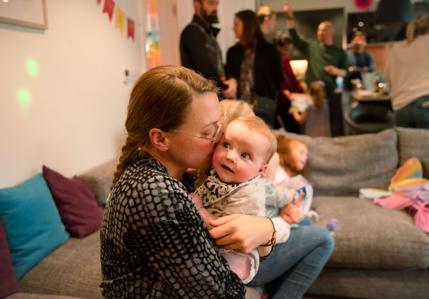 An adult holds and snuggles with a baby while sitting on a couch at a party with decorations in the background.