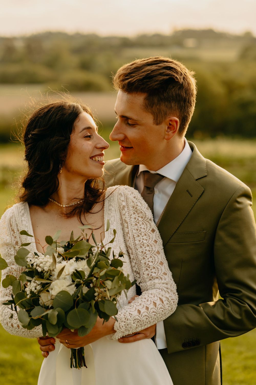 Newlywed couple shares intimate moments during golden hour photoshoot in rustic outdoor setting.