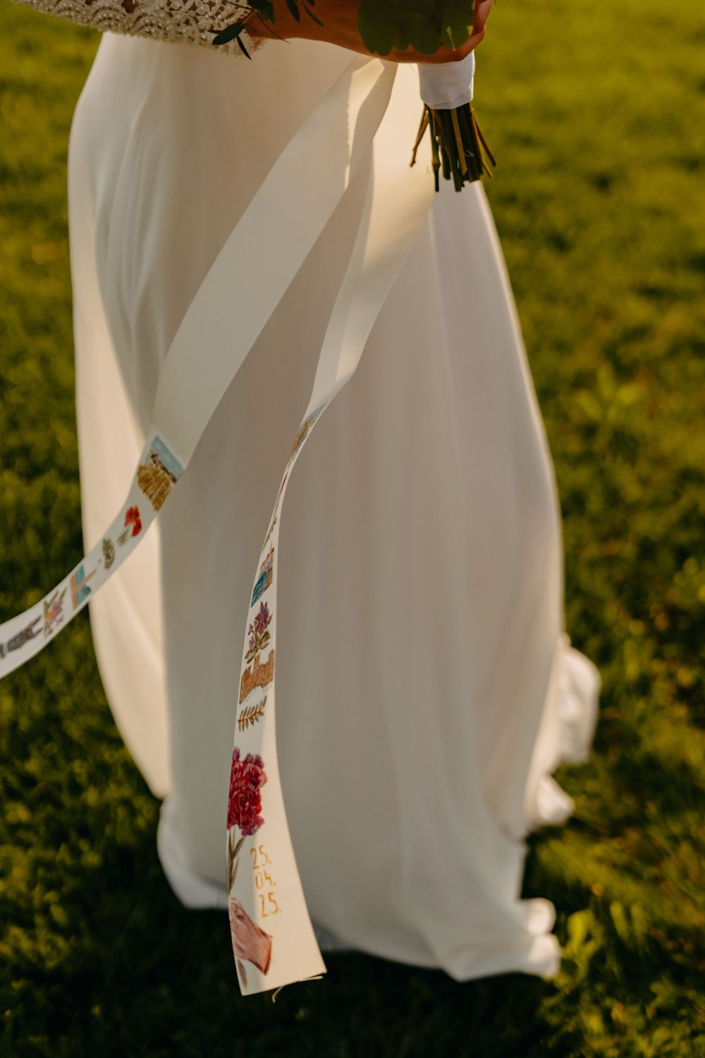A white wedding dress skirt flows gracefully in the sunlight on green grass during an outdoor ceremony.