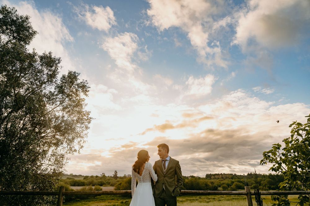 Scenic sunset wedding portraits in a lush garden landscape with dramatic golden sky and clouds.