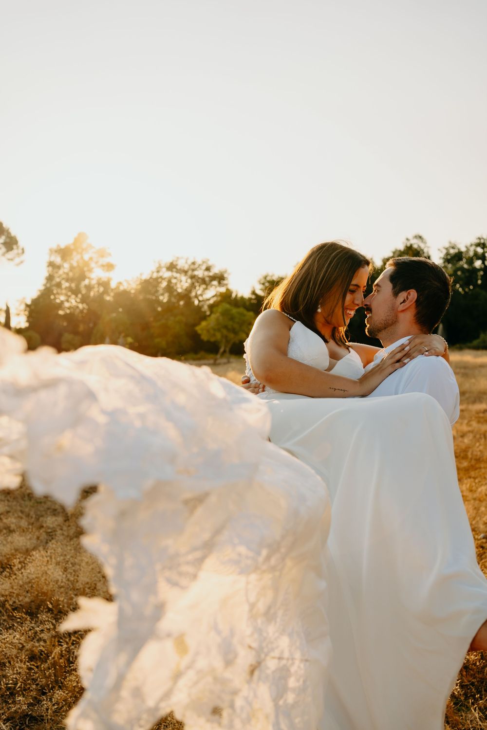 A romantic sunset wedding photo with a flowing white dress against a golden field of grass during magic hour.