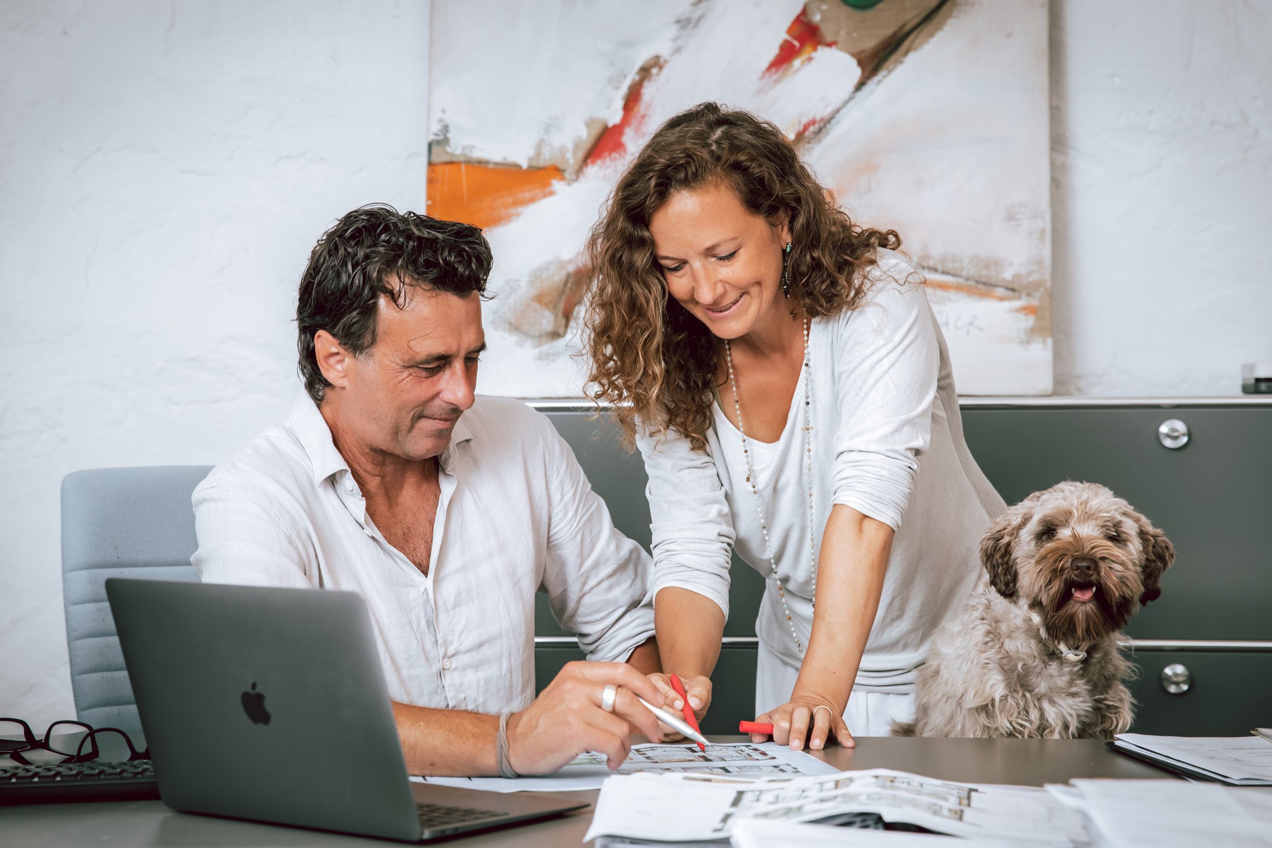 candid portrait of a smiling architect couple working at a desk with a laptop and their small dog in a Mallorca home.