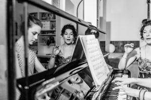 Black and white photo of a young woman as a reflexion in a piano with her female piano teacher.
