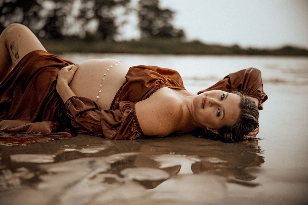 Woman in brown dress reclining in shallow coastal waters.