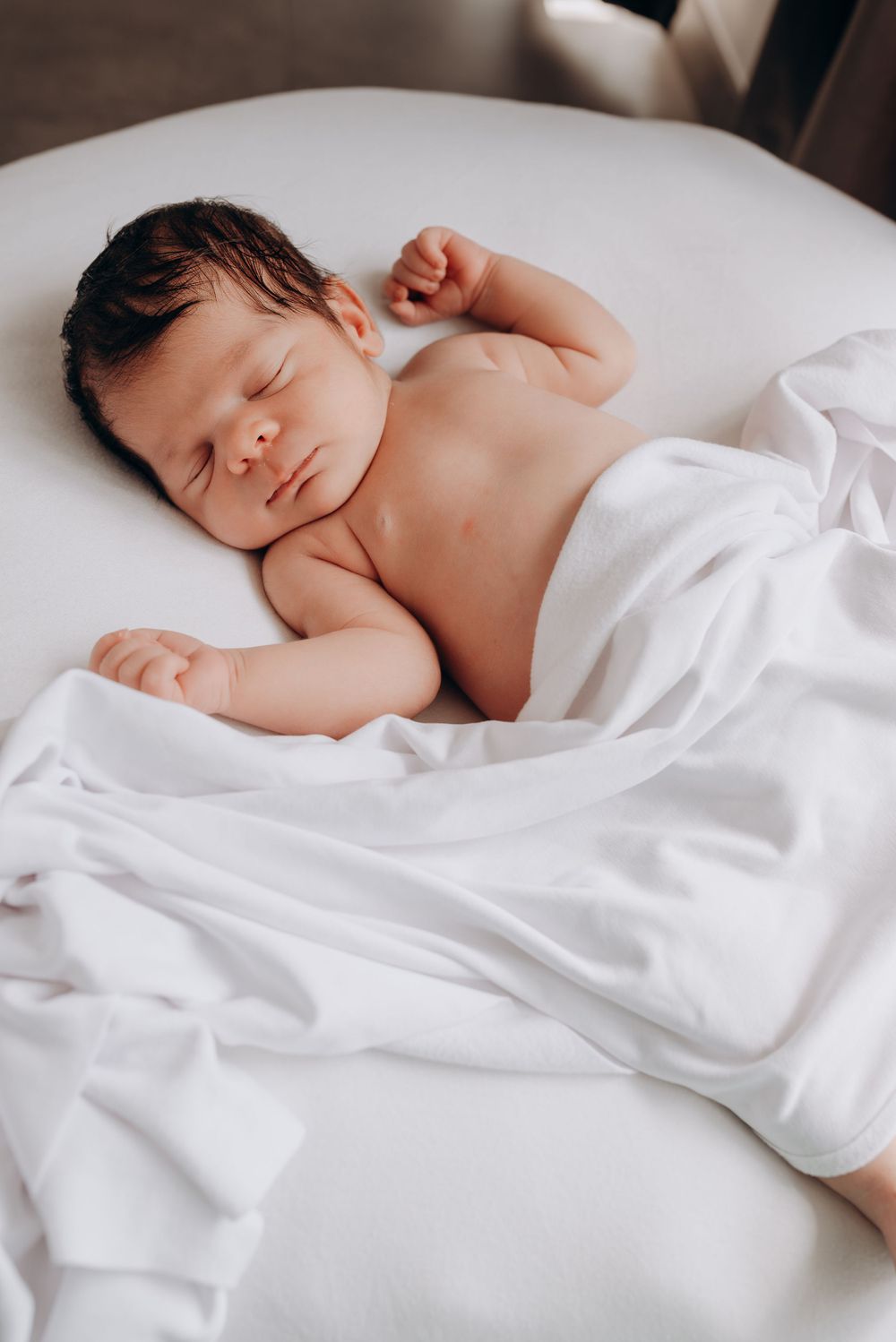 Sleeping newborn baby on white sheets in natural window light.