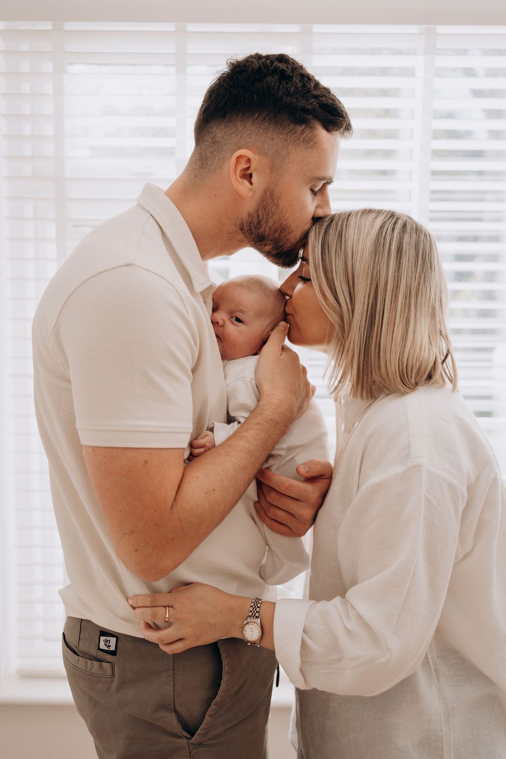 Intimate family moment captured in white room with window blinds.