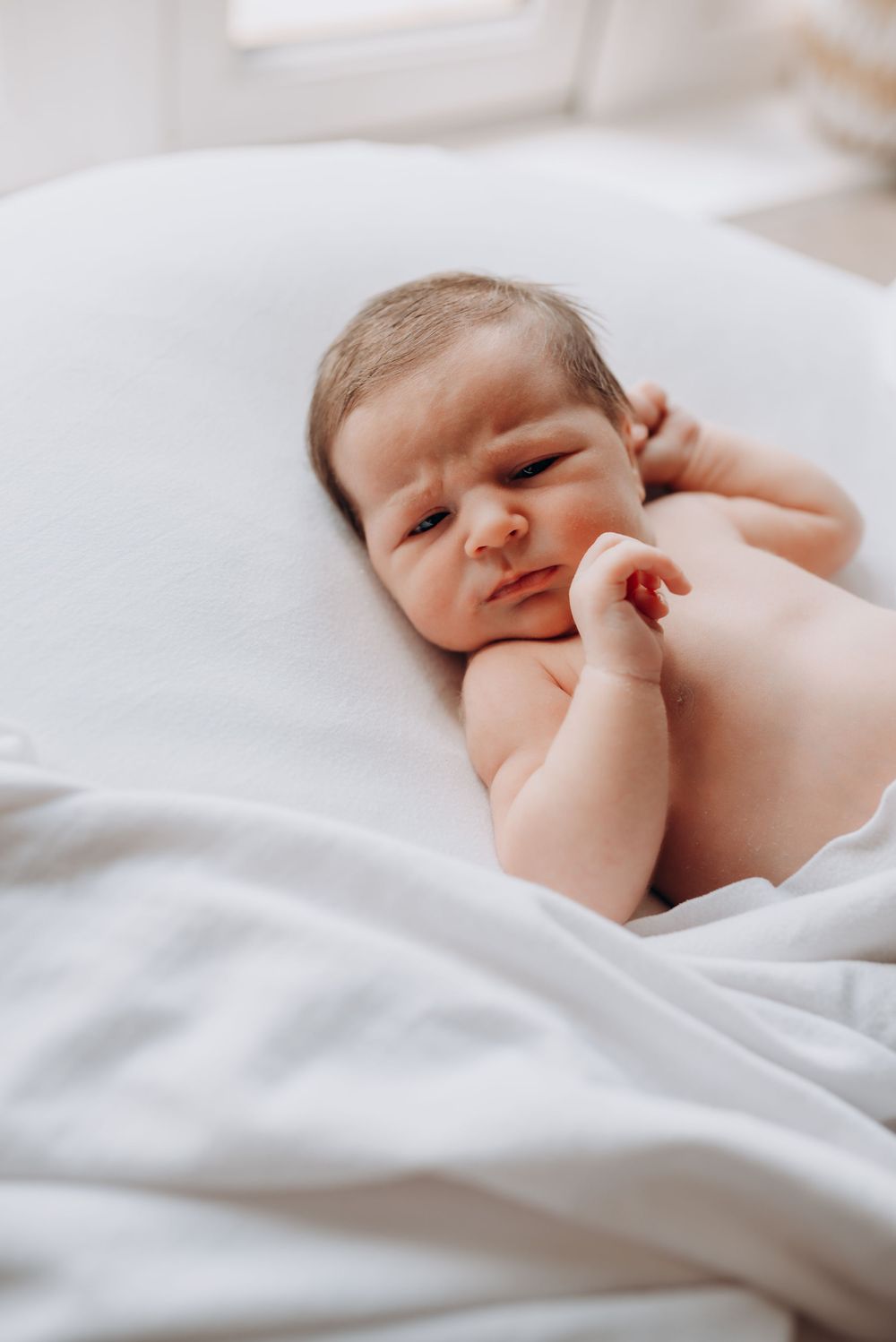 Newborn baby lying on white bedding in natural light.