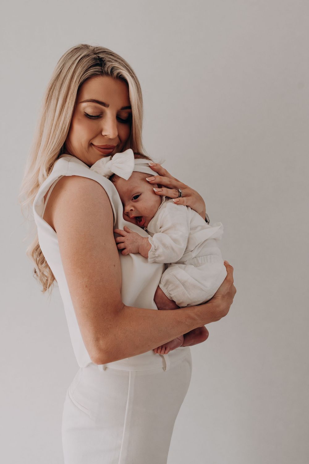 Tender moment between mother and newborn baby in white against neutral background.