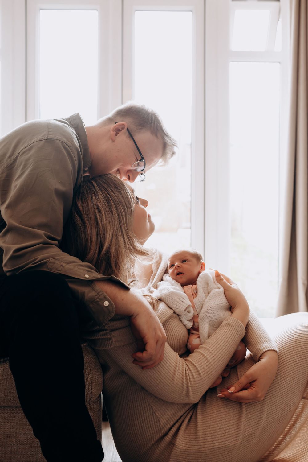 Family shares intimate moment with newborn by bright window.
