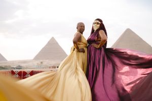 Flowing dresses billow dramatically against the backdrop of the Great Pyramids of Giza in Egypt at sunset.
