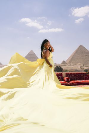 Flowing yellow dress creates dramatic movement against Egyptian pyramid landscape.